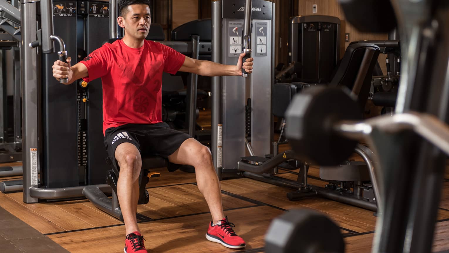 Man in red shirt sits on bench, prepares to pull weights in Fitness Centre