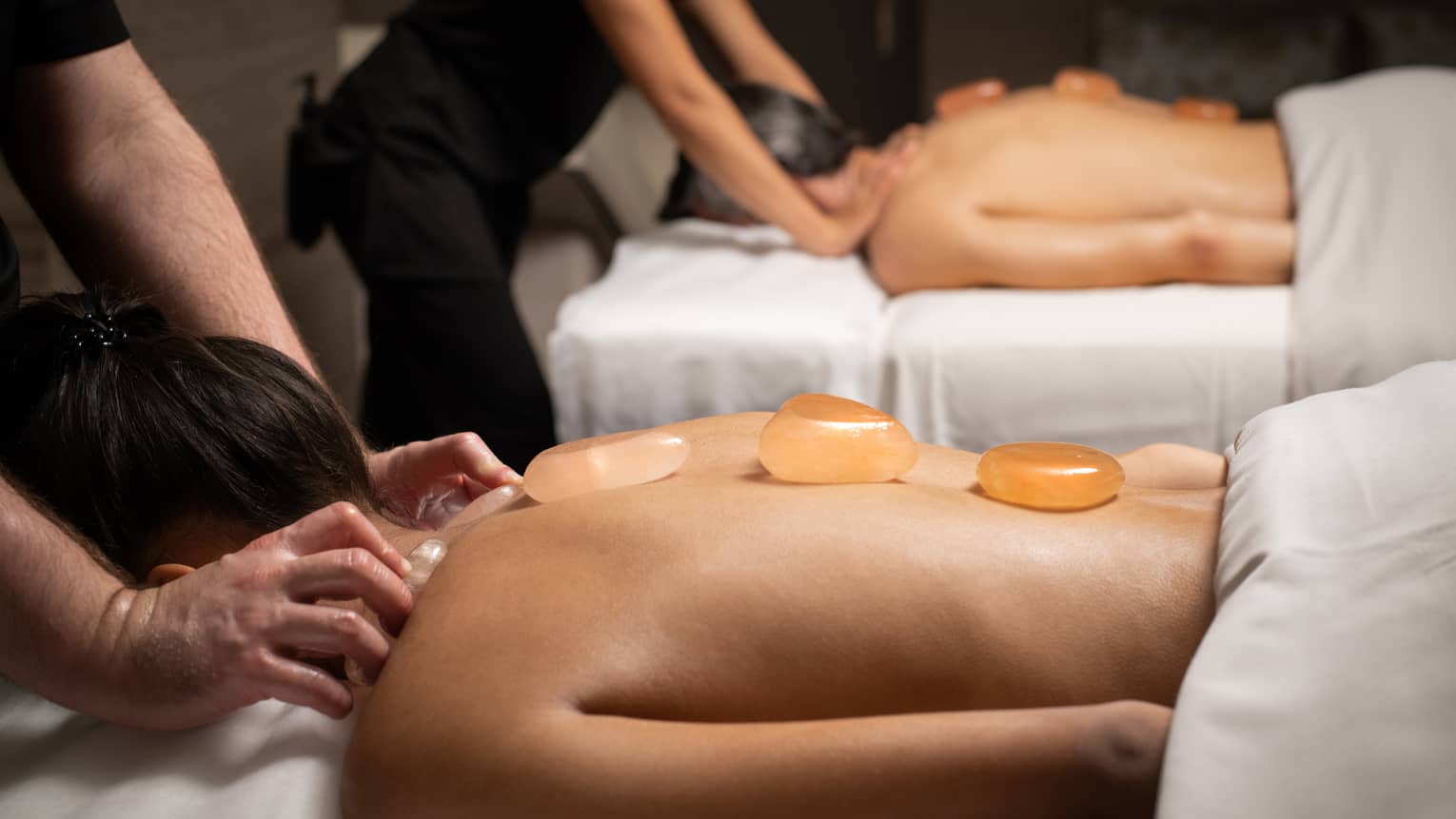Two people getting a massage with small stones on their backs.