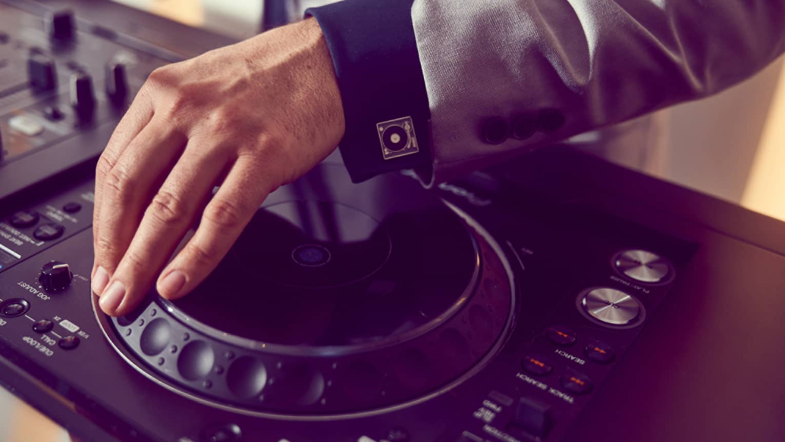The hand of a DJ touching a small turntable on a soundboard.