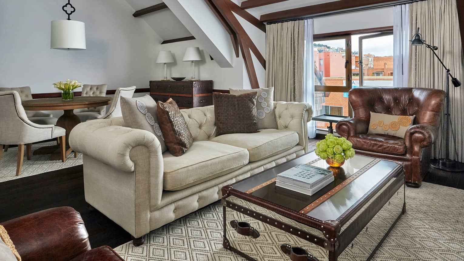 Penthouse Suite living room with sofas, trunk-style coffee table, in front of dining table and chairs, beamed ceiling