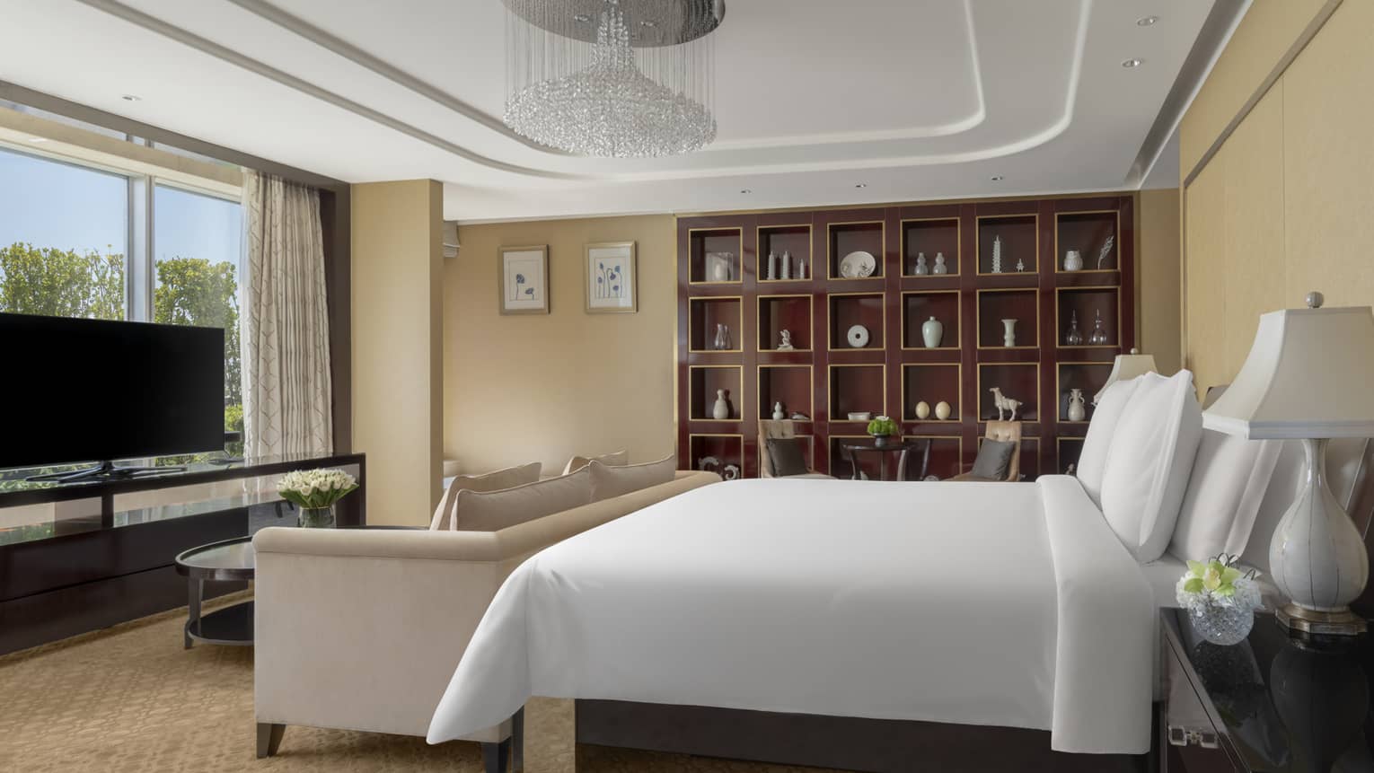 Hotel suite bedroom, with king bed, chandelier, sofa, TV and built-in dark-wood shelves