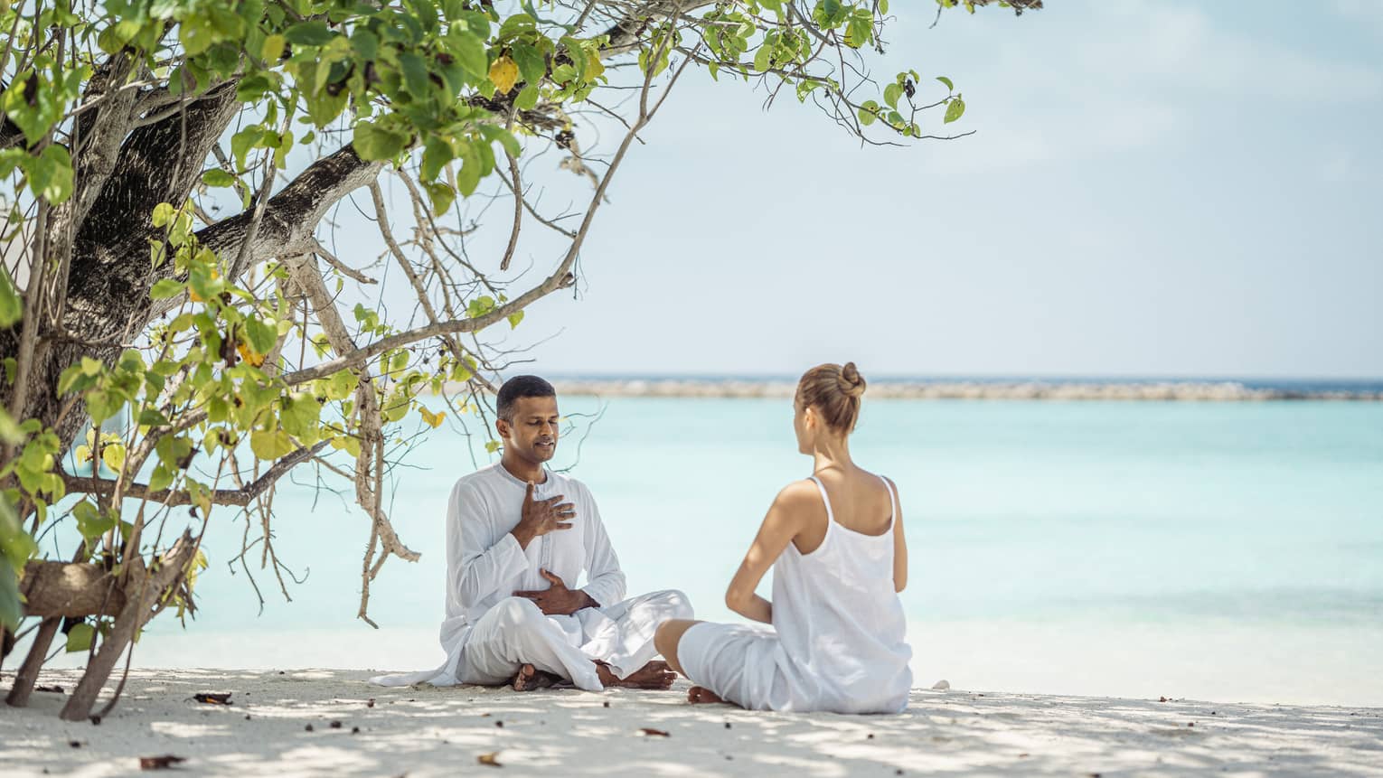 Dr. Arun K. Tomson practises breathing exercises with female guest on the beach under the shade of a tree