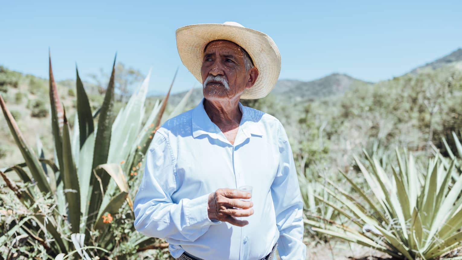 Person wearing a hat and a blue button down shirt standing outside.