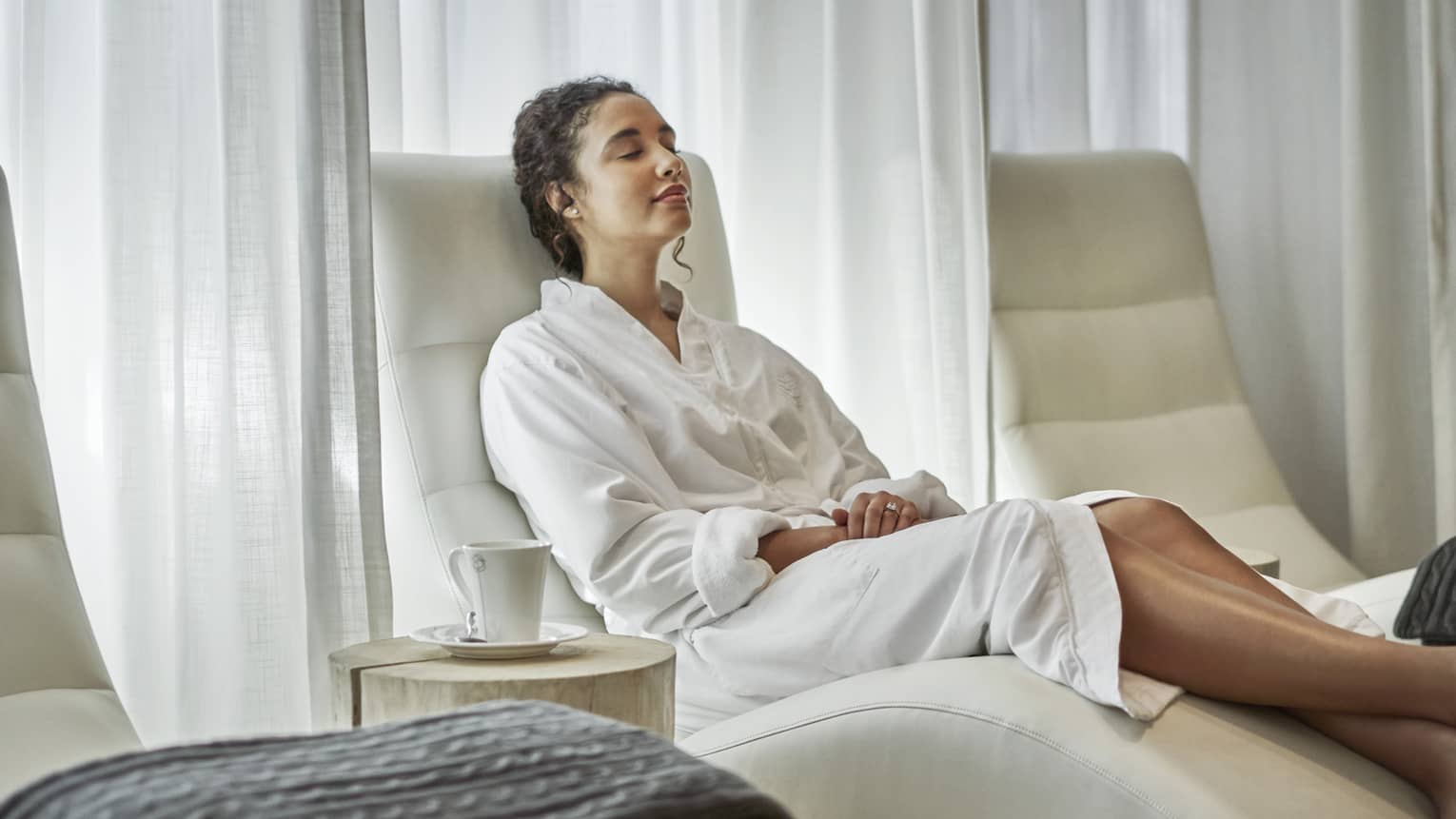 A woman in a white robe lounges on a curved chair after a spa treatment.