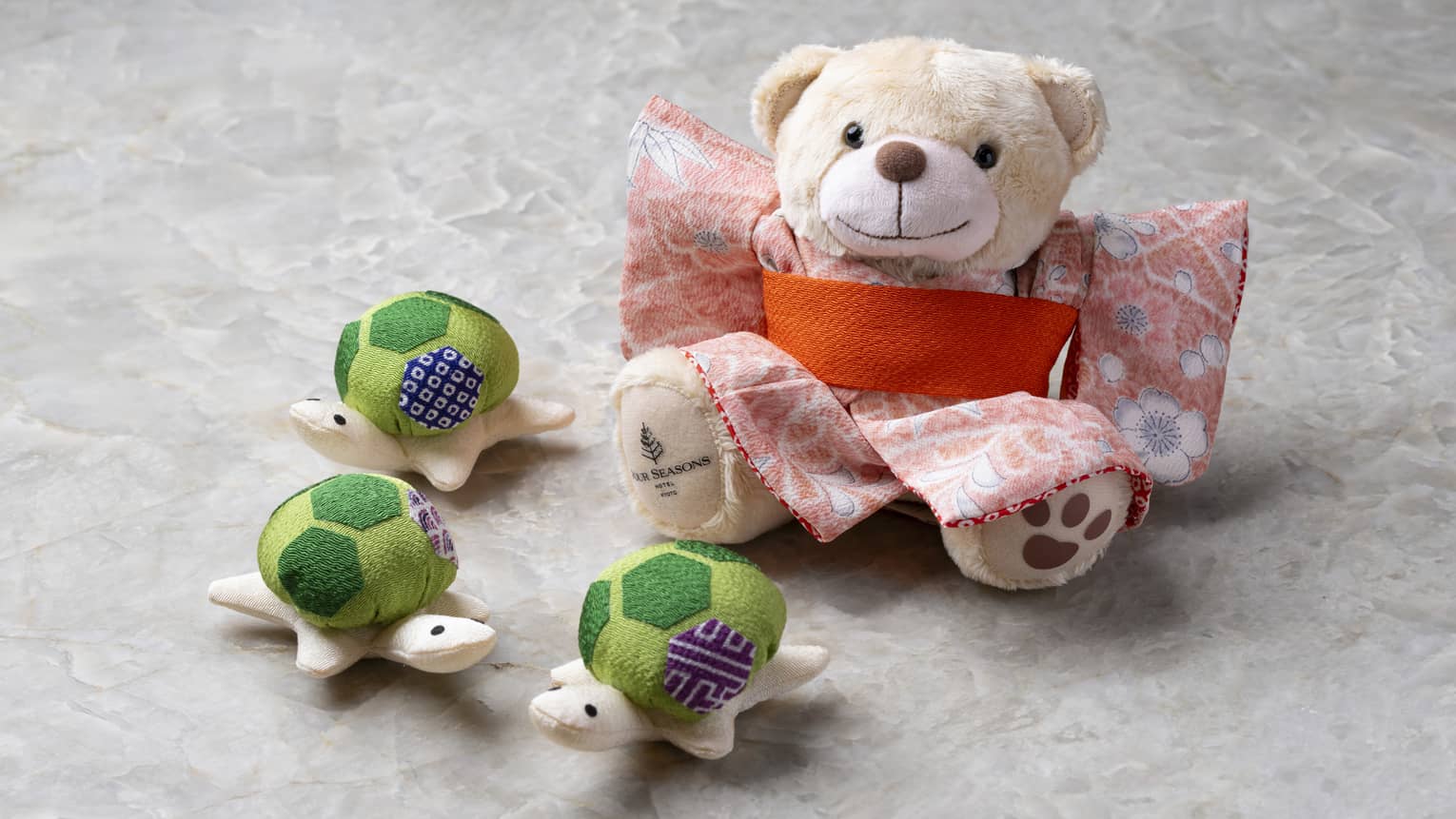 Cream-coloured stuffed bear in kimono and three stuffed turtles with green patterned shells