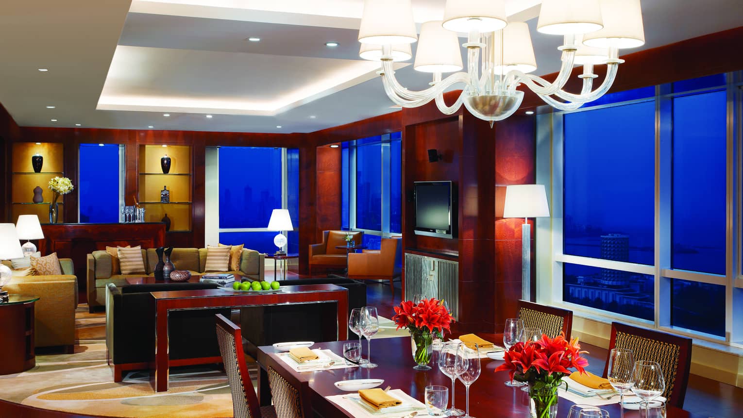Presidential Suite long dining table under chandelier, seating area, corner windows at night