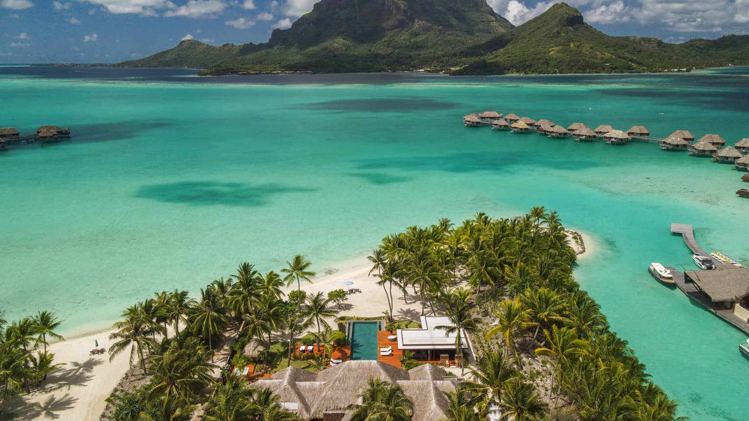 Aerial view of Bora Bora villa on edge of turquoise lagoon, looking out to overwater bungalows and mountains