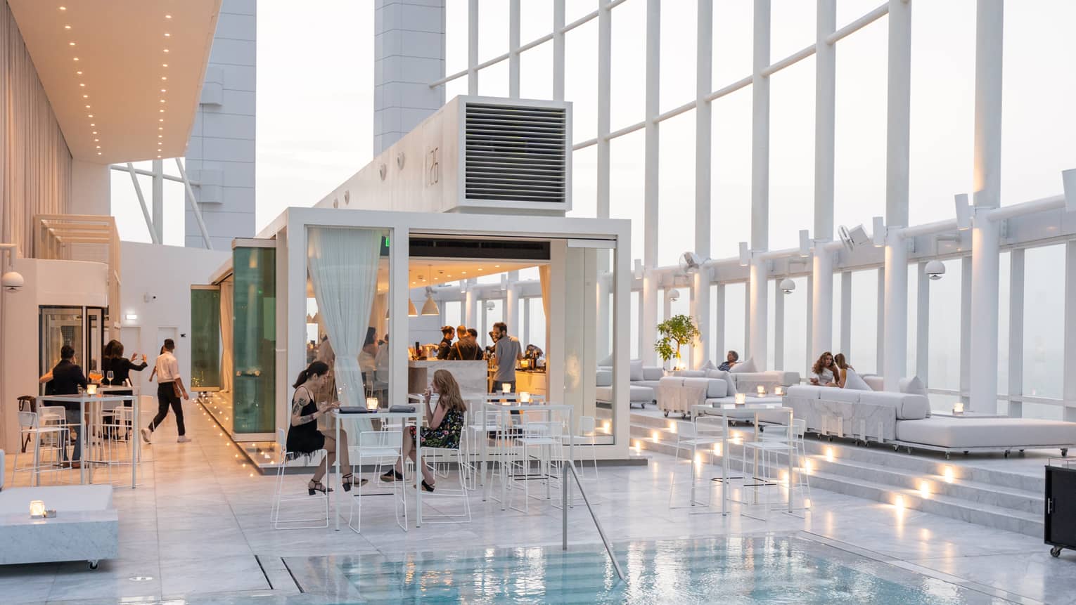 People mingle around a contemporary white bar next to pool