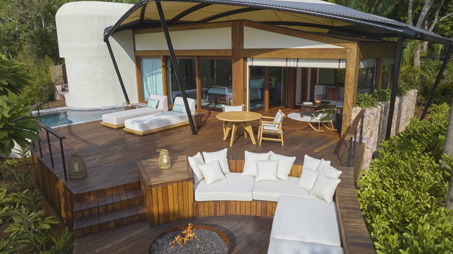 Luxury tent nestled within tropical forest, with outdoor lounge seating, fire pit and plunge pool