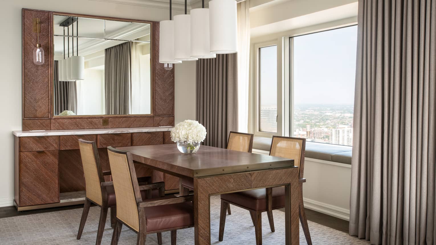 Wood dining table with four chairs, buffet with mirror, white cylindrical light fixture, window with city view