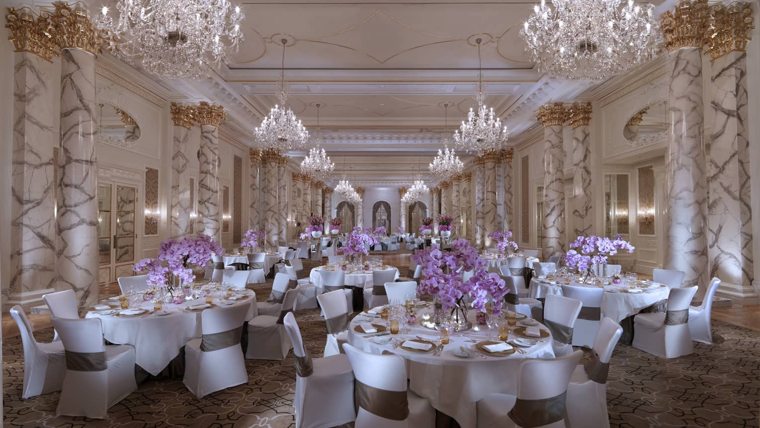 Elegant ballroom with banquet tables under tall marble pillars, crystal chandeliers 