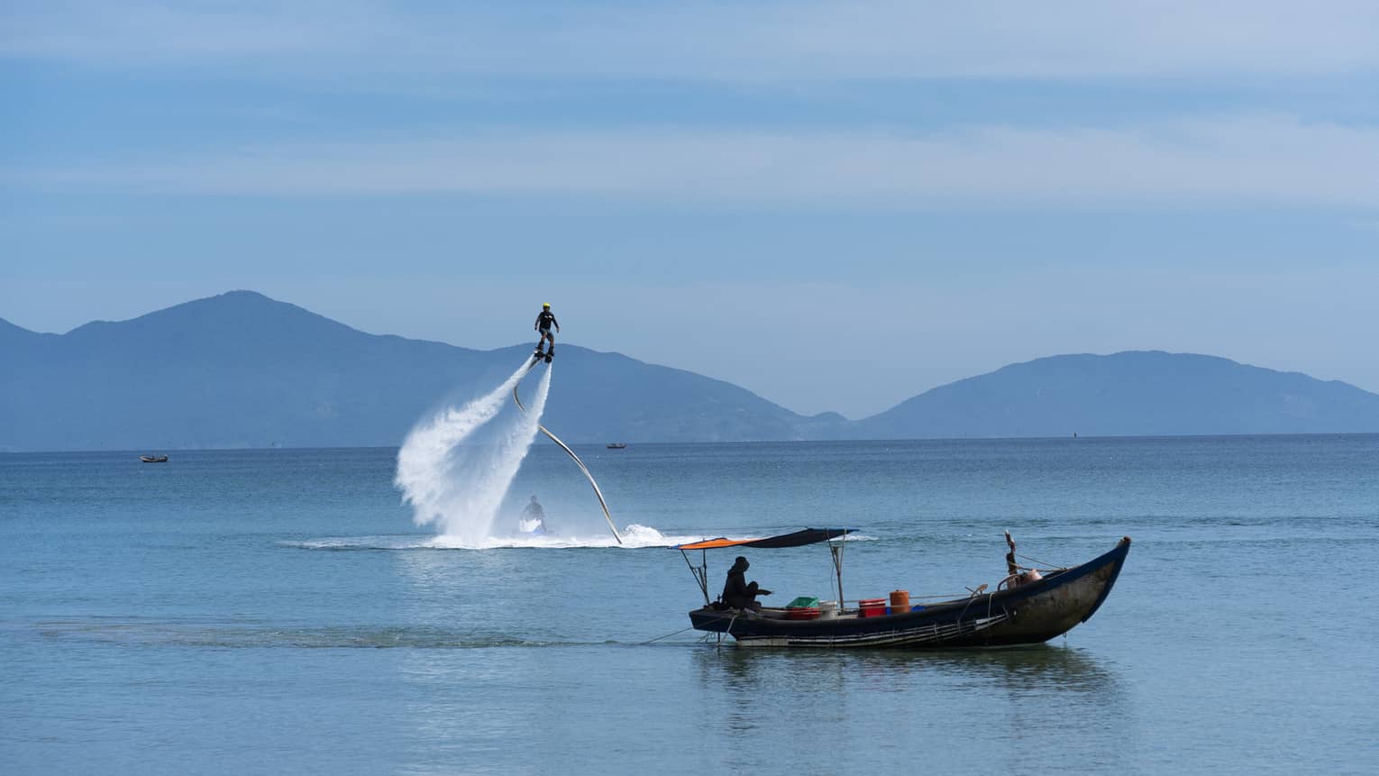 Man on X-jetpack and man in fishing boat out on the open water, mountain views and blue skies