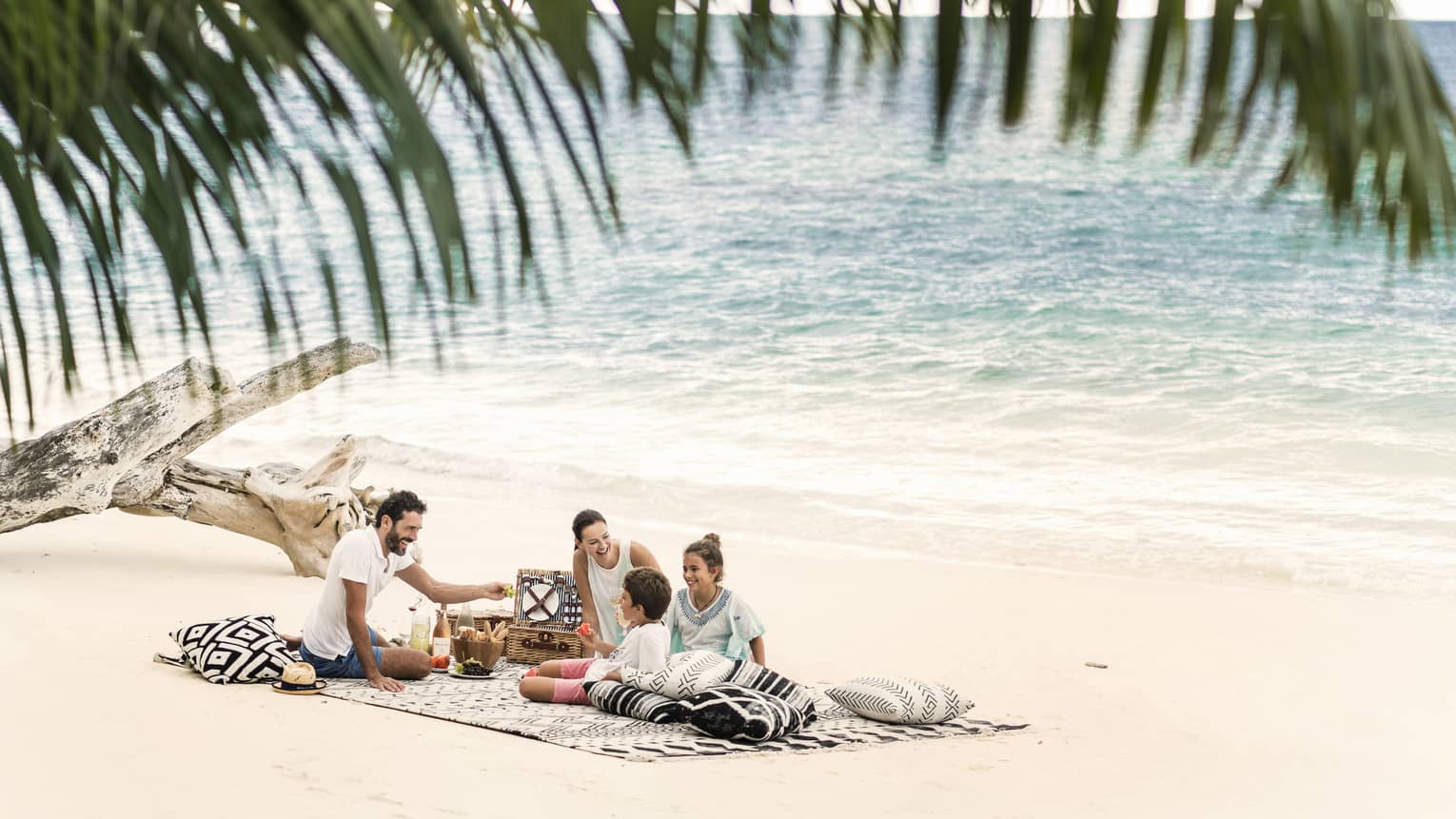 A man, woman and two children picnic on the beach just a couple feet away from the ocean. 