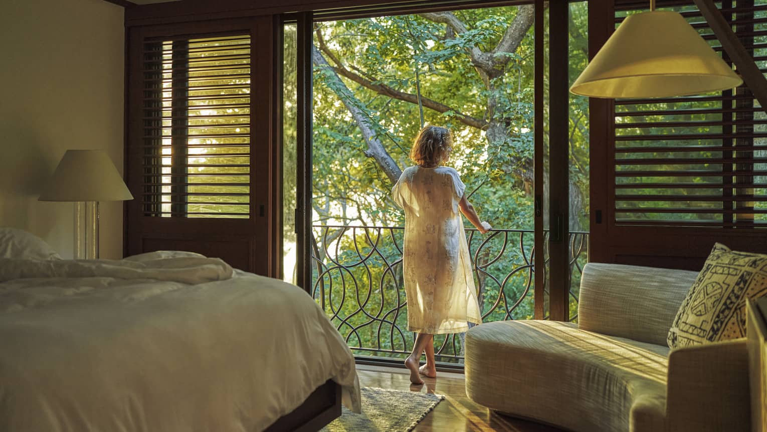 Woman stands at balcony from bedroom, looking out to jungle