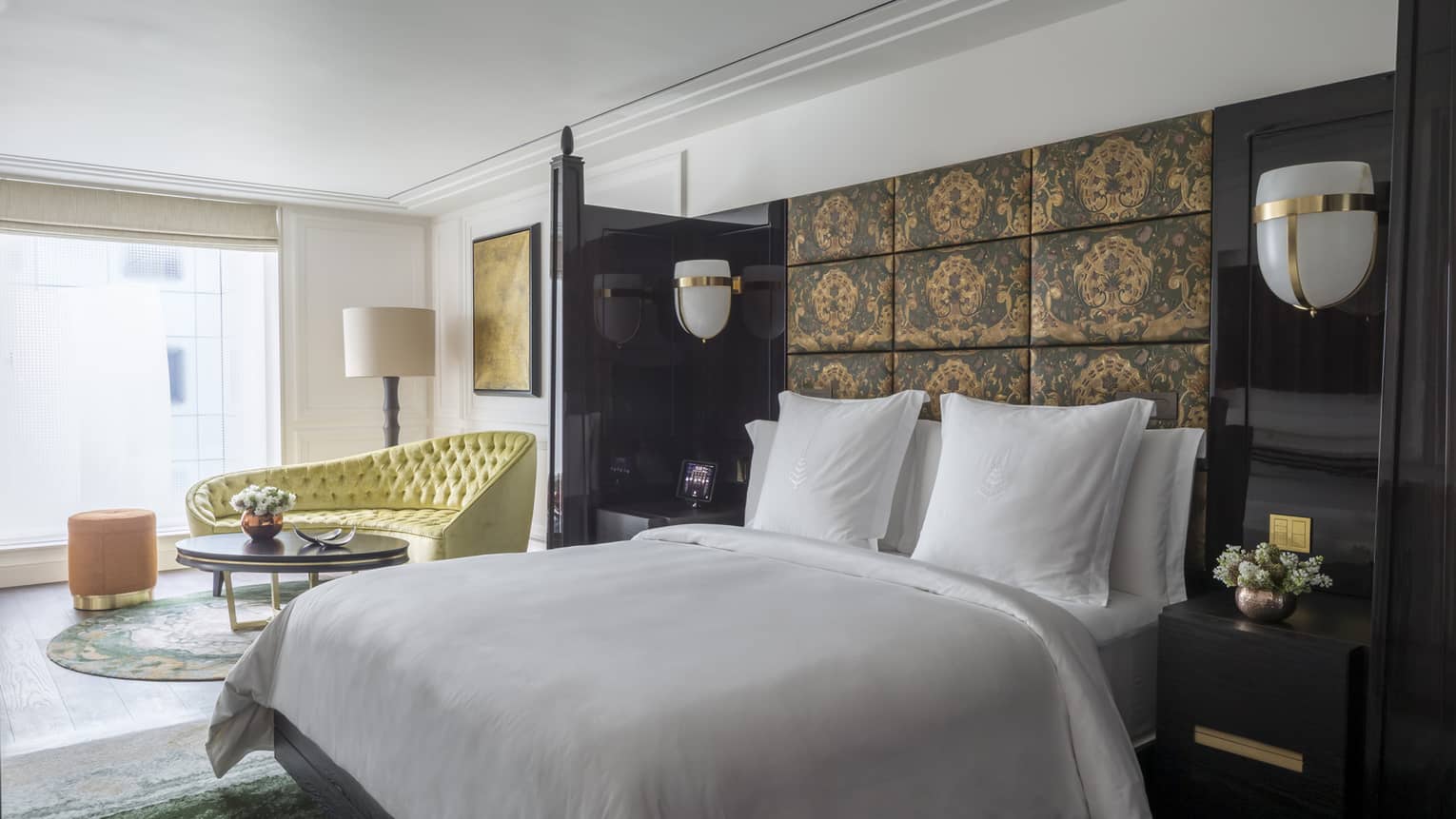 White bed against dark fabric-panelled wall with view of living area