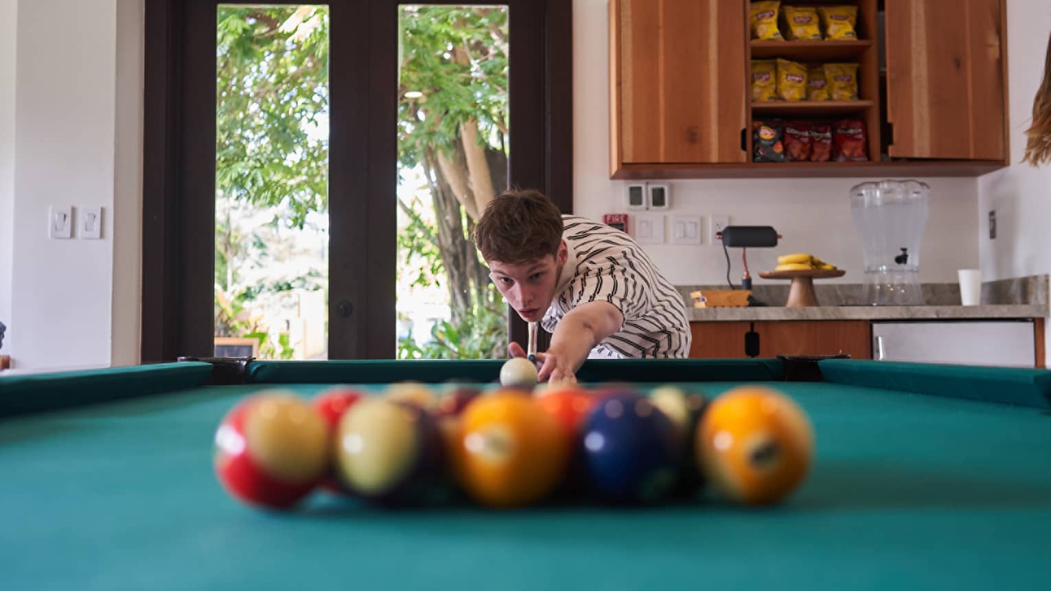 Teenage boy setting up to break a set of billard balls on a teal pool table