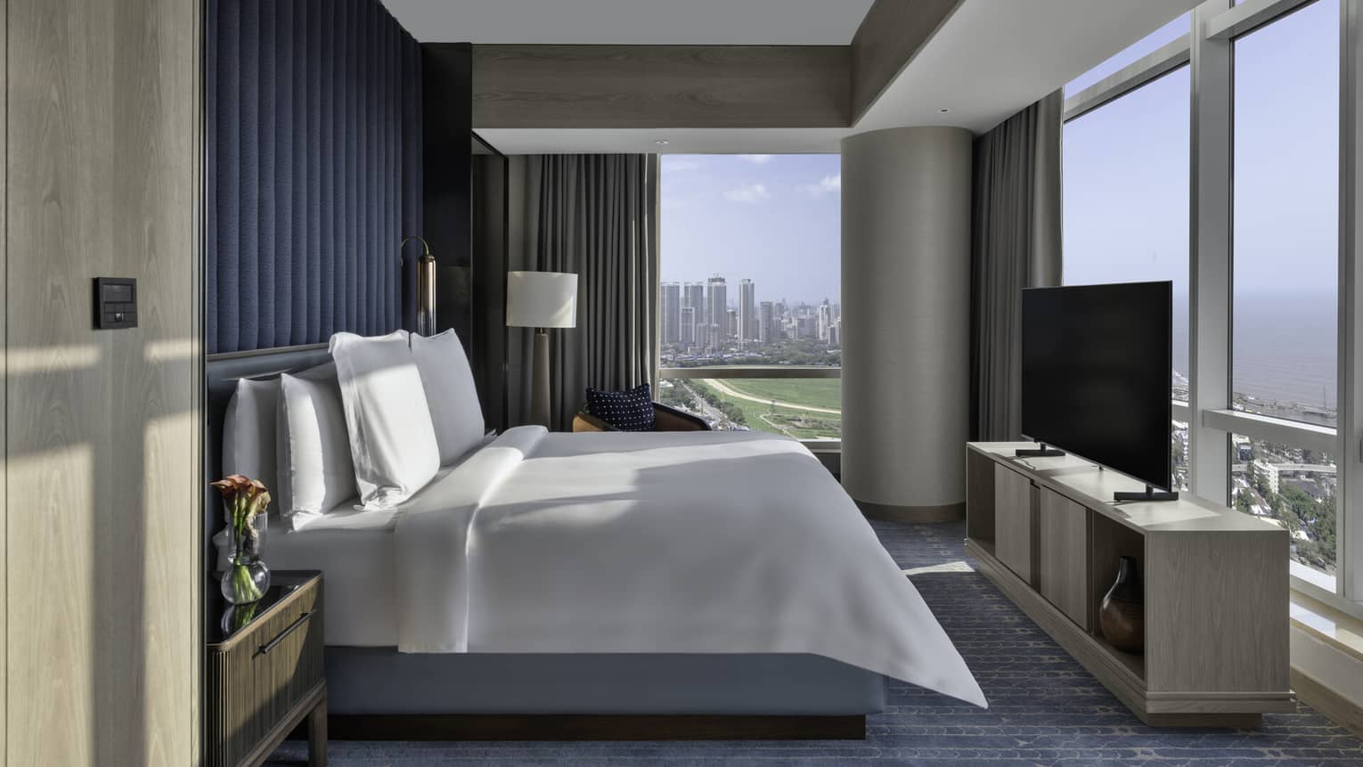 Renovated Deluxe Sea-View Room with bed and white linens, flat screen TV on stand, teal carpet and accent wall, floor-to-ceiling windows with city views