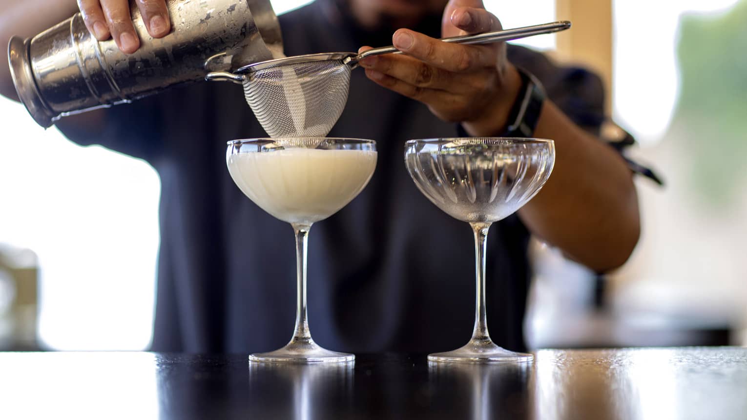 A bartender strains a chilled cocktail into two glasses