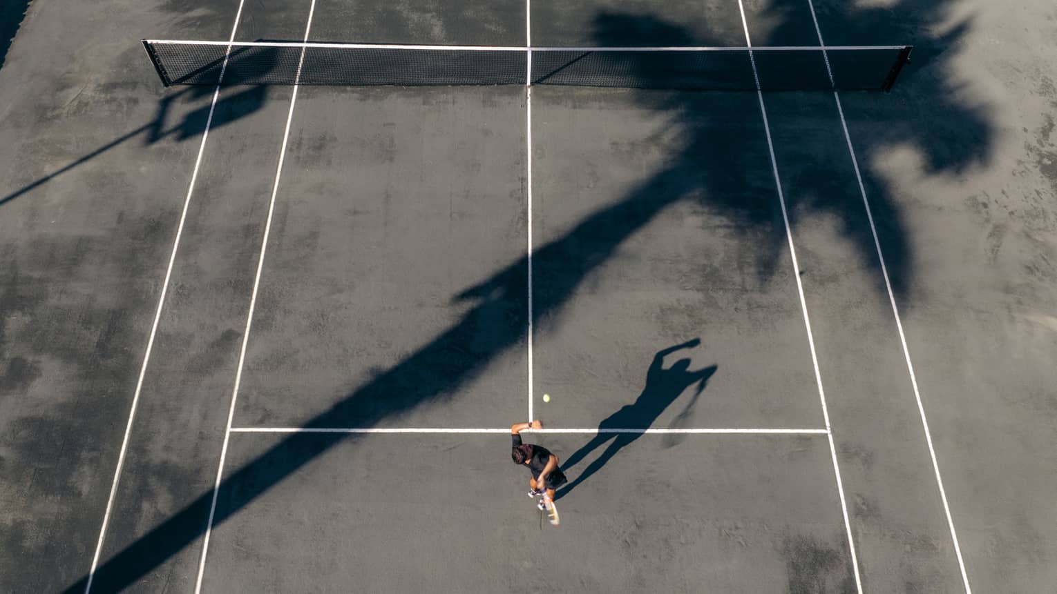 Aerial view of person serving the ball on a clay tennis court