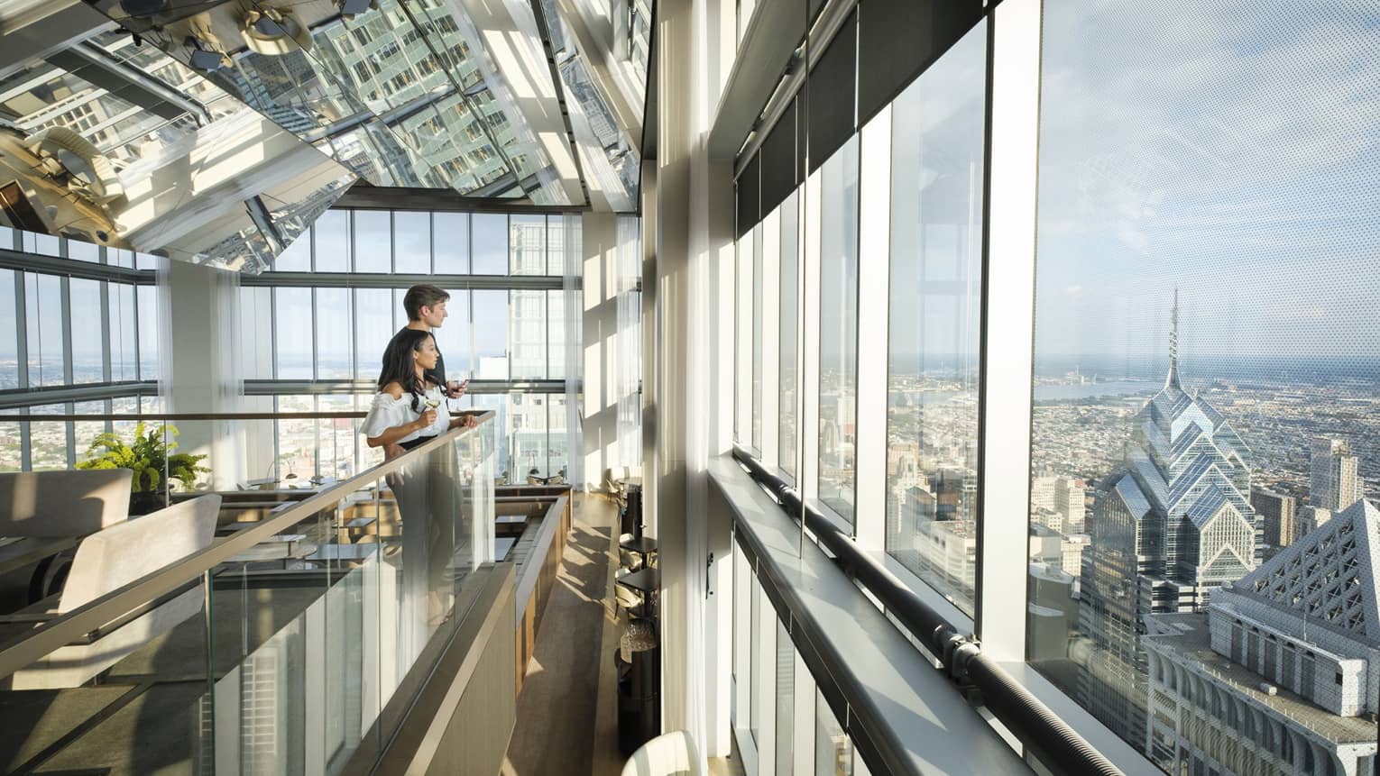 A man and woman looking out of a large window in a restaurant on a high floor of a building.
