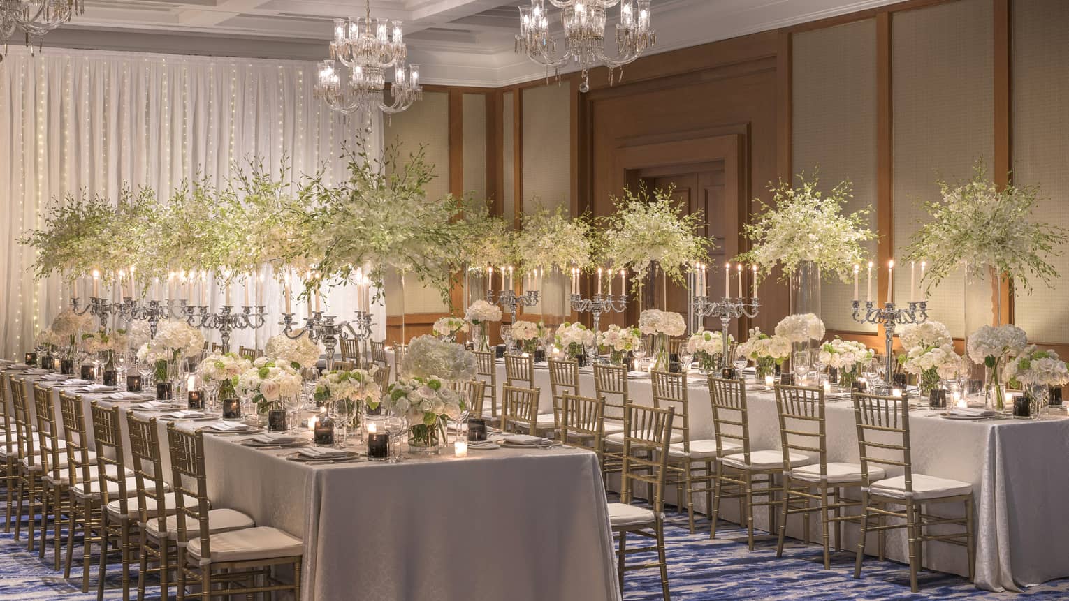 Two long tables are adorned with candelabras and tall and short bouquets of white flowers