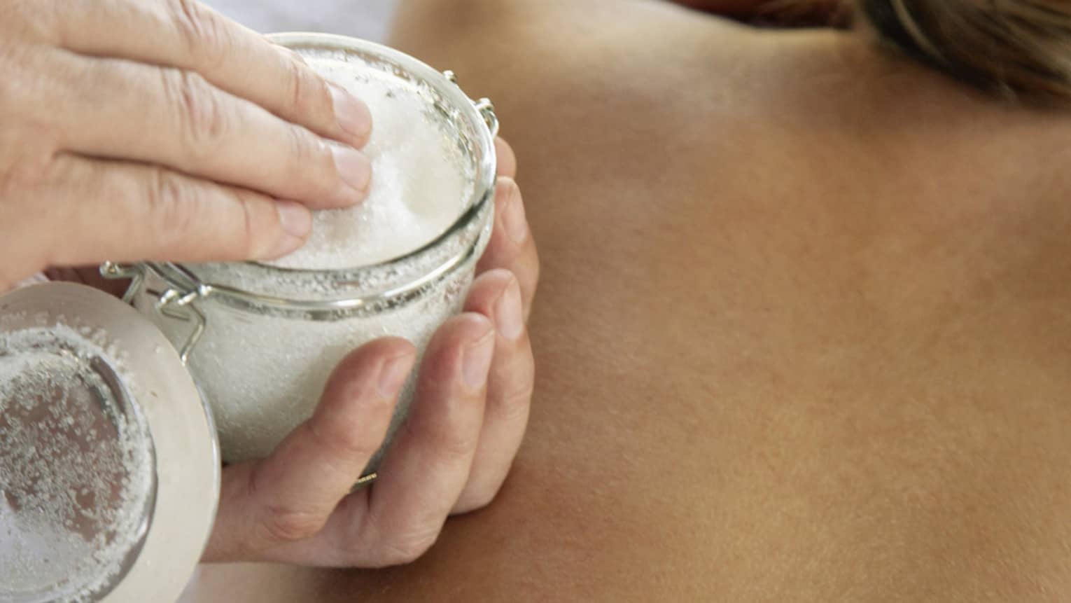 Jar of sea salt scrub above woman's bare back in spa