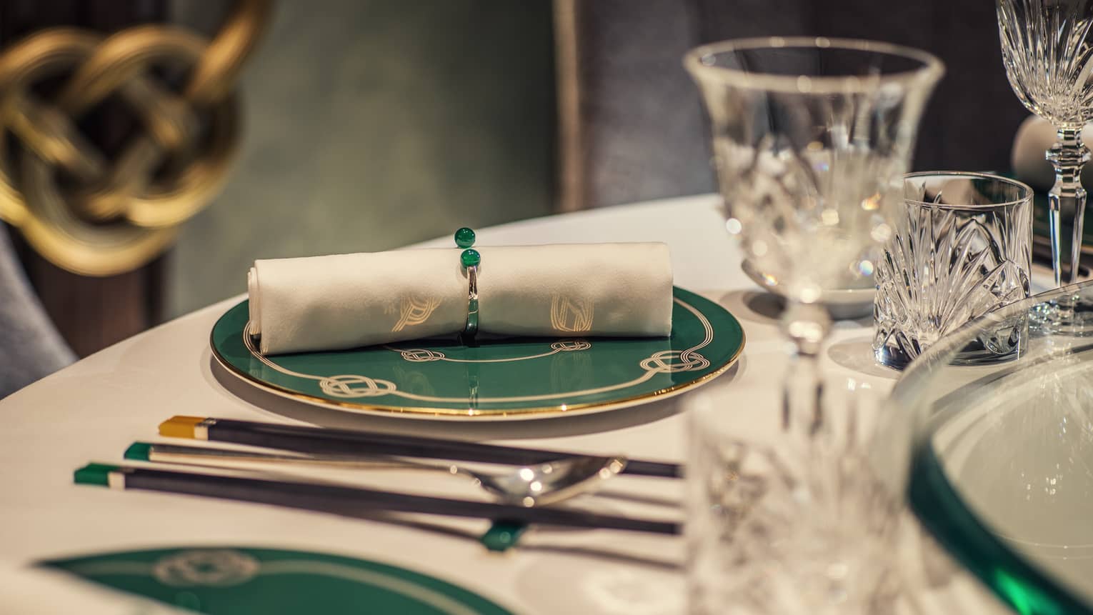 Yu Yuan close-up of rolled white napkin on green-and-gold plate, crystal glasses