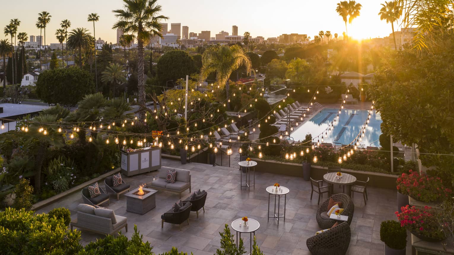 An outdoor seating area with hanging fairy lights and a fire pit near chairs and small tables.