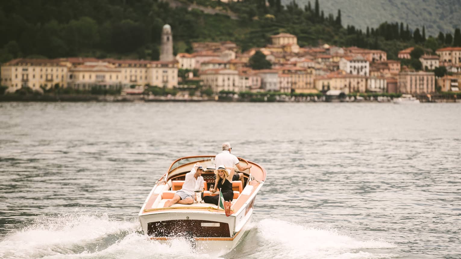 Couple laugh, drink Champagne on back of powerboat on Lake Como