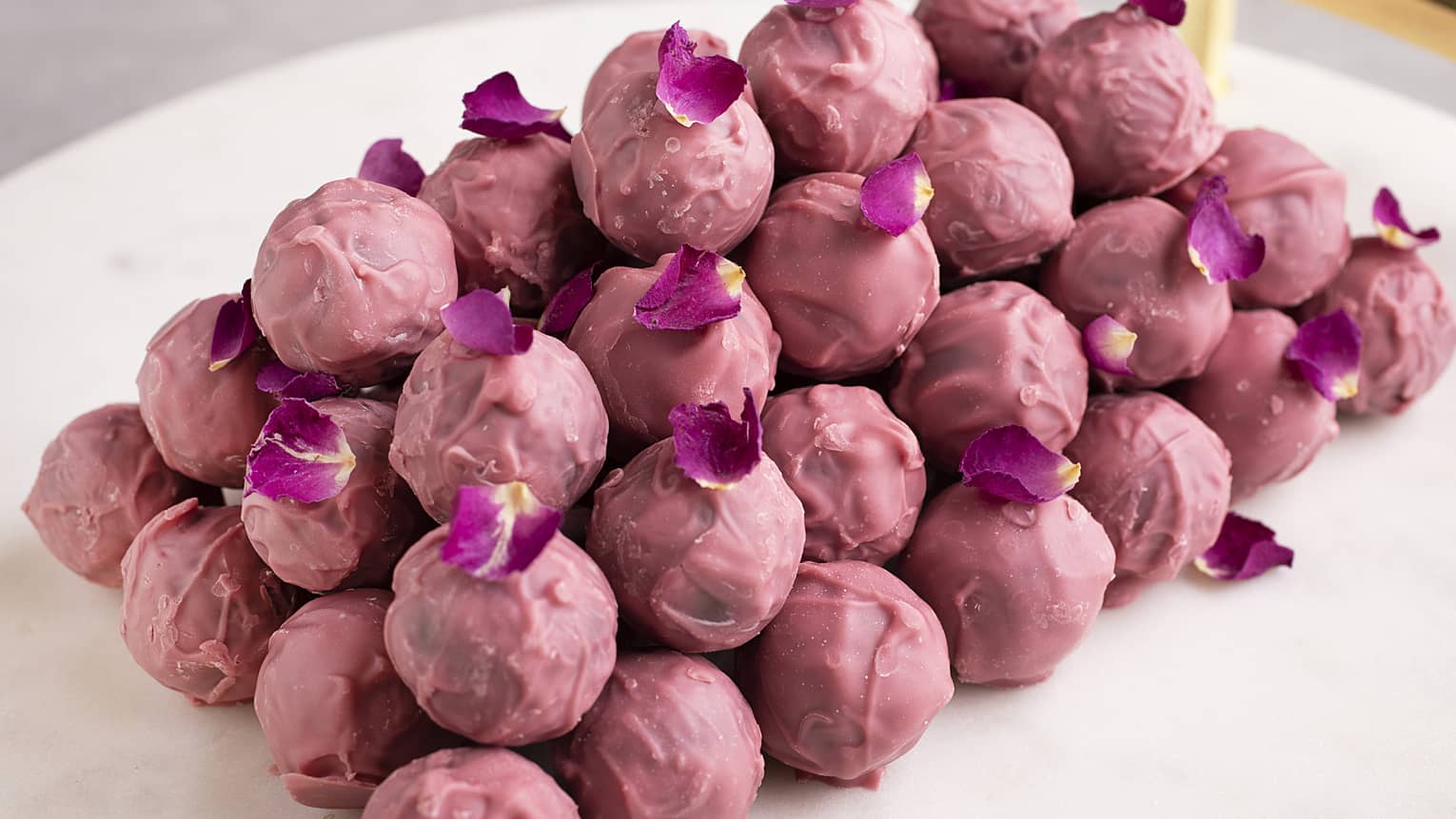 A stack of rose-colored chocolate pralines sprinkled with purple flower petals