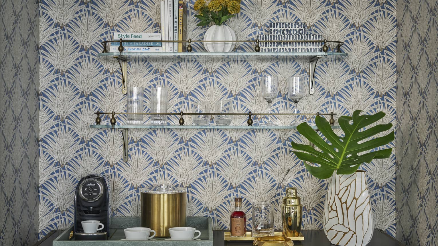 A bar set up on a sideboard, set against a wall with two shelves and tropical wallpaper