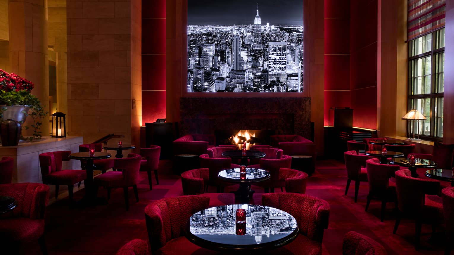Black-and-white city skyline image above red velvet lounge chairs, cocktail tables