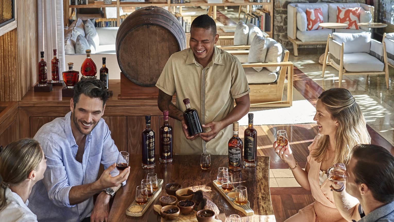 A bartender smiles as four guests sample different kinds of rum at a table set with bowls of chocolate, glasses and bottles.