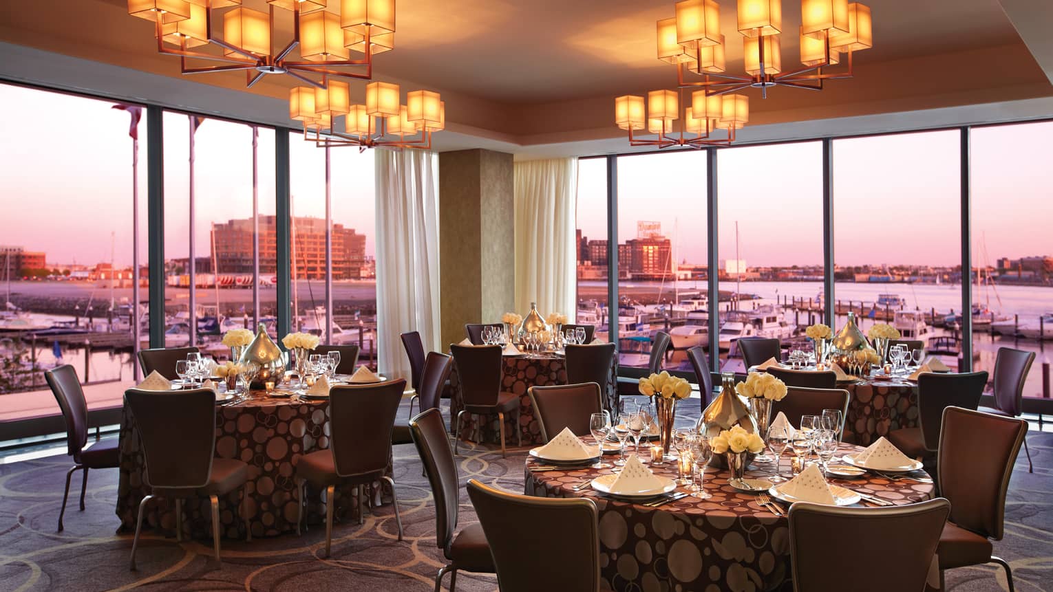 Cerulean banquet room dining tables by corner floor-to-ceiling windows, sunset views