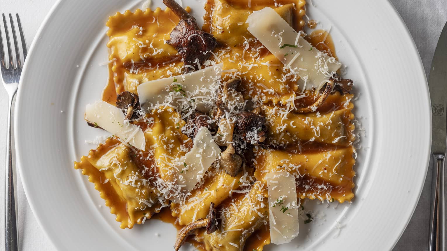 Ravioli doppi served on a white, round dish and topped with Parmigiano Reggiano and mushrooms