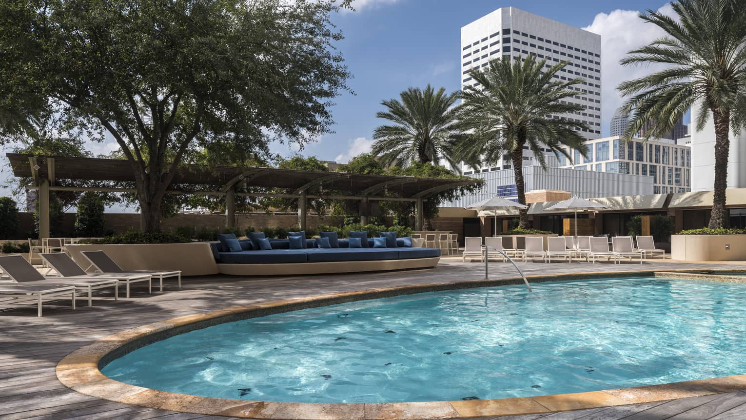 View across sunny outdoor swimming pool to patio, row of lounge chairs and palm trees 