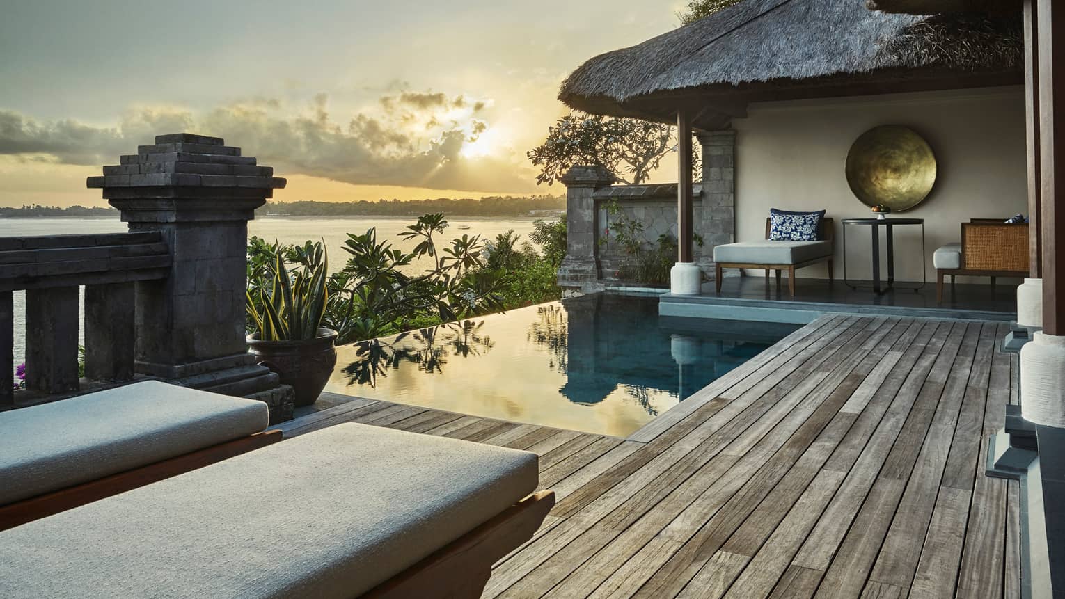 Ocean sunset reflecting on private villa swimming pool, palm trees, thatched roof, lounge chairs