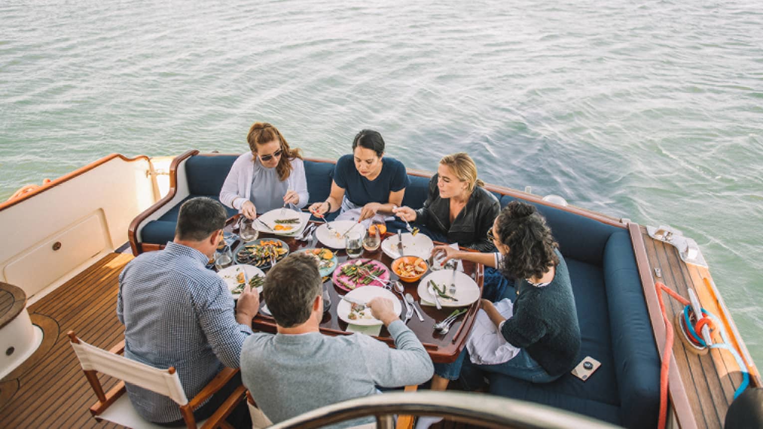 Group of friends dine at table at end of boat on water 