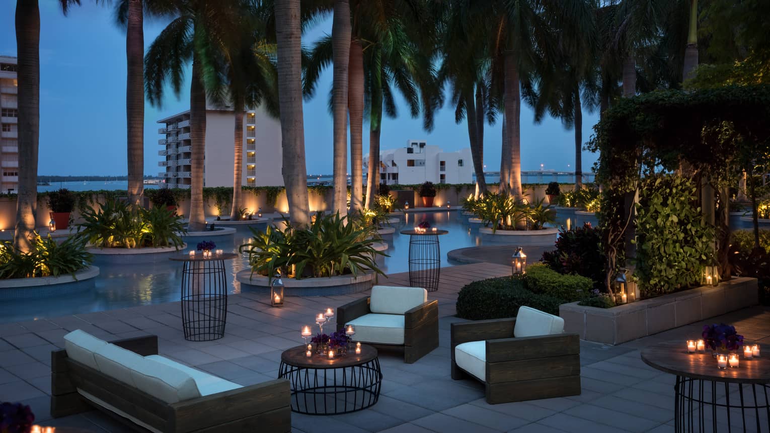 Plush white patio sofas and chairs, candle-lit tables under palm trees at night