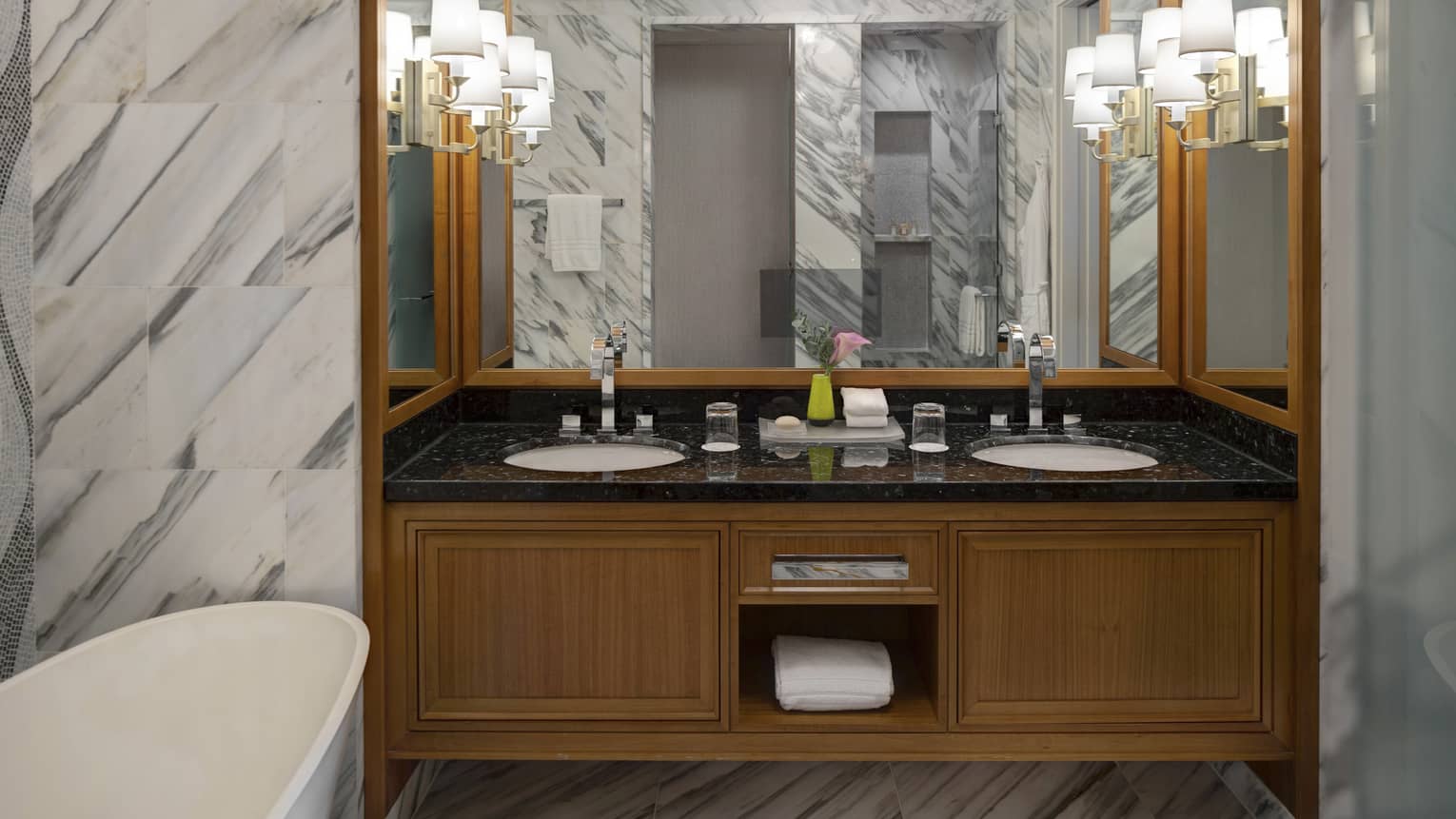 Bathroom with double vanity, sconces, white tub, marble walls