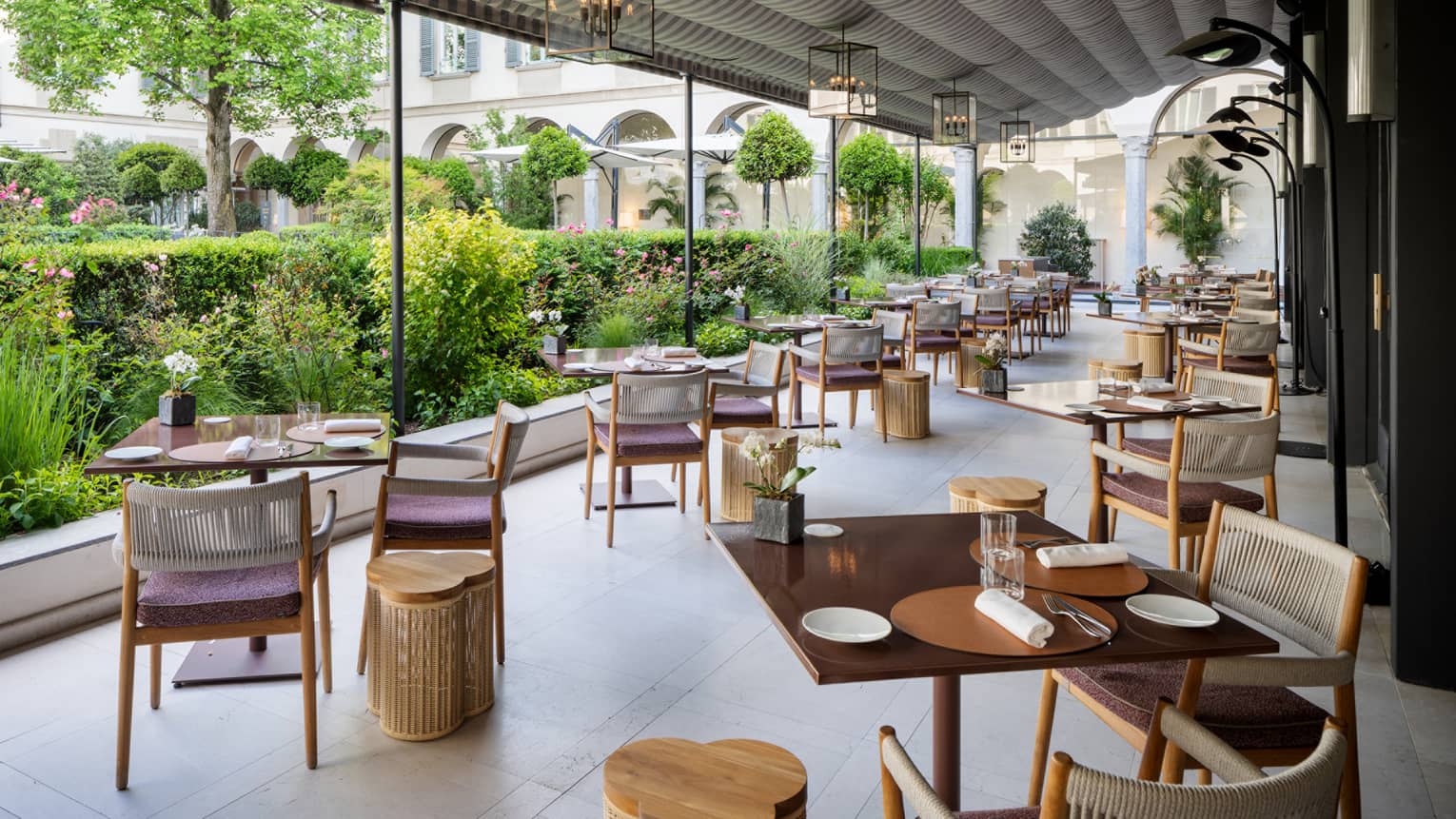 Covered terrace dining area lined with two rows of square tables looking out to verdant courtyard