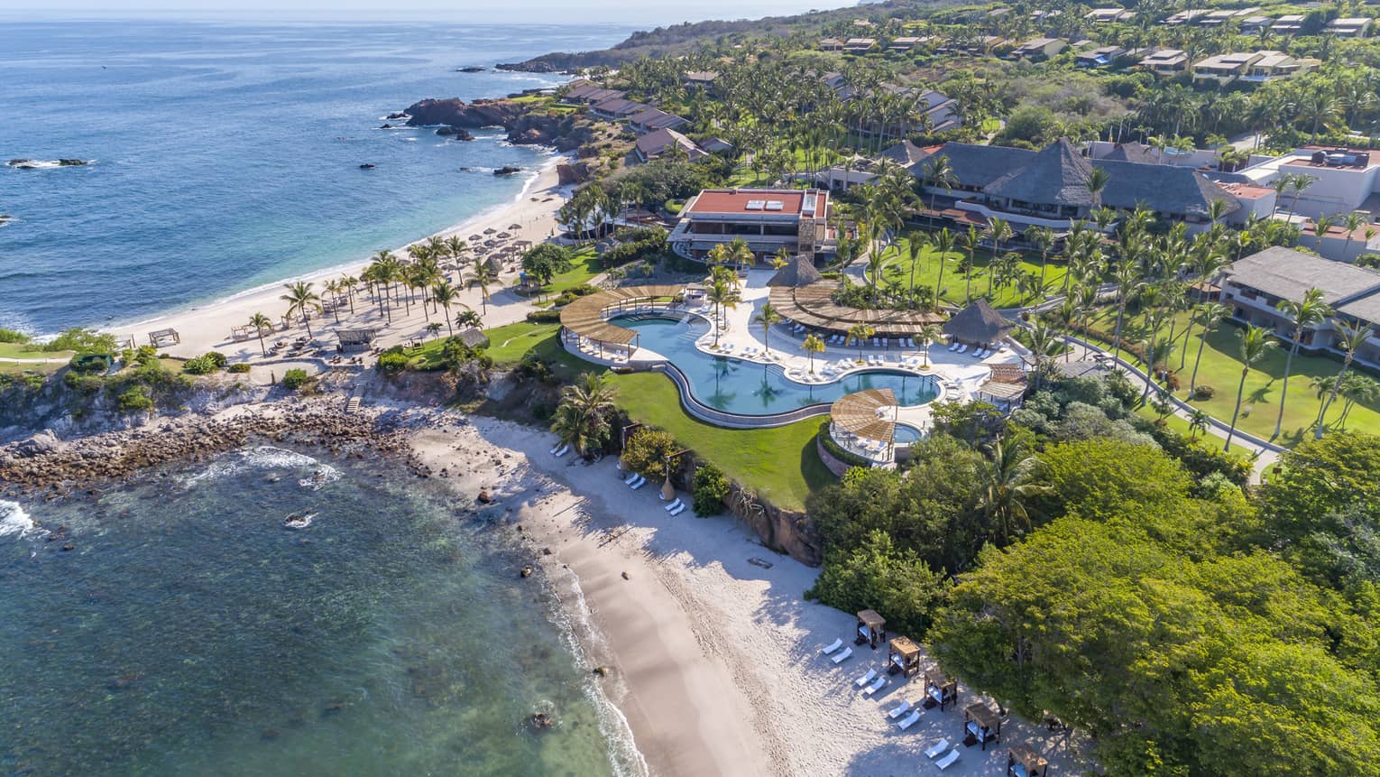 An aerial view of a beach shore with a large property on it with an outdoor pool.