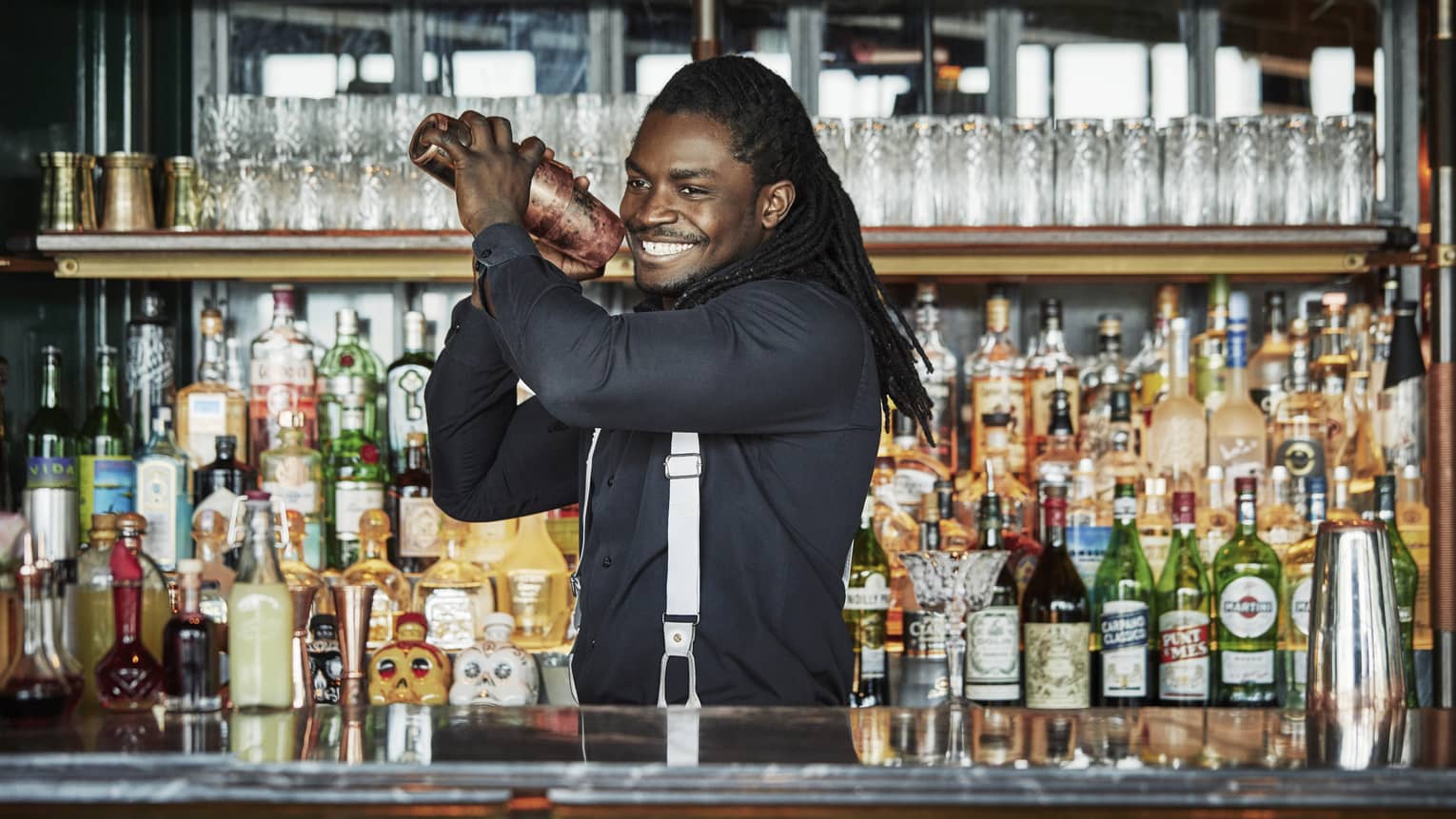 Smiling Butcher & Still bartender shakes cocktail behind bar, liquor display