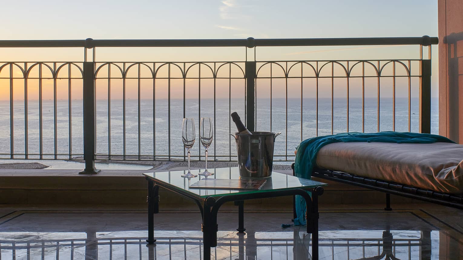 Suite balcony with longue chair, side table with champagne, sea views at sunset