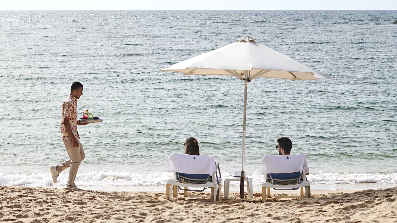 a couple lounges on the beach in alexandria while a four seasons staff serves them refreshments