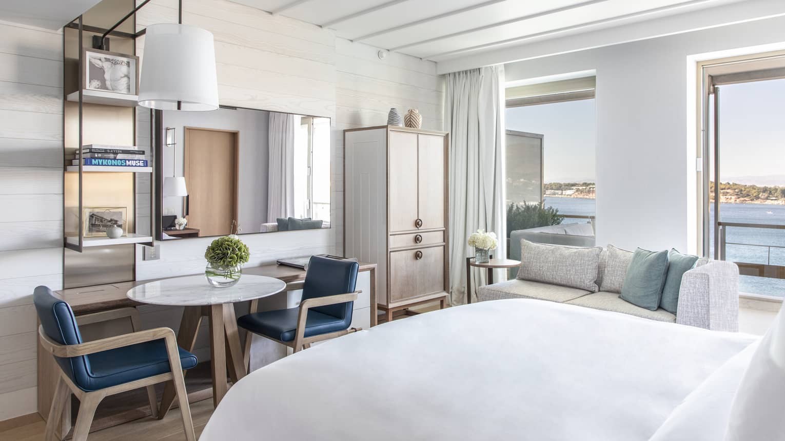 Bedroom with small table, two blue chairs, wall-mounted lamp, sea views