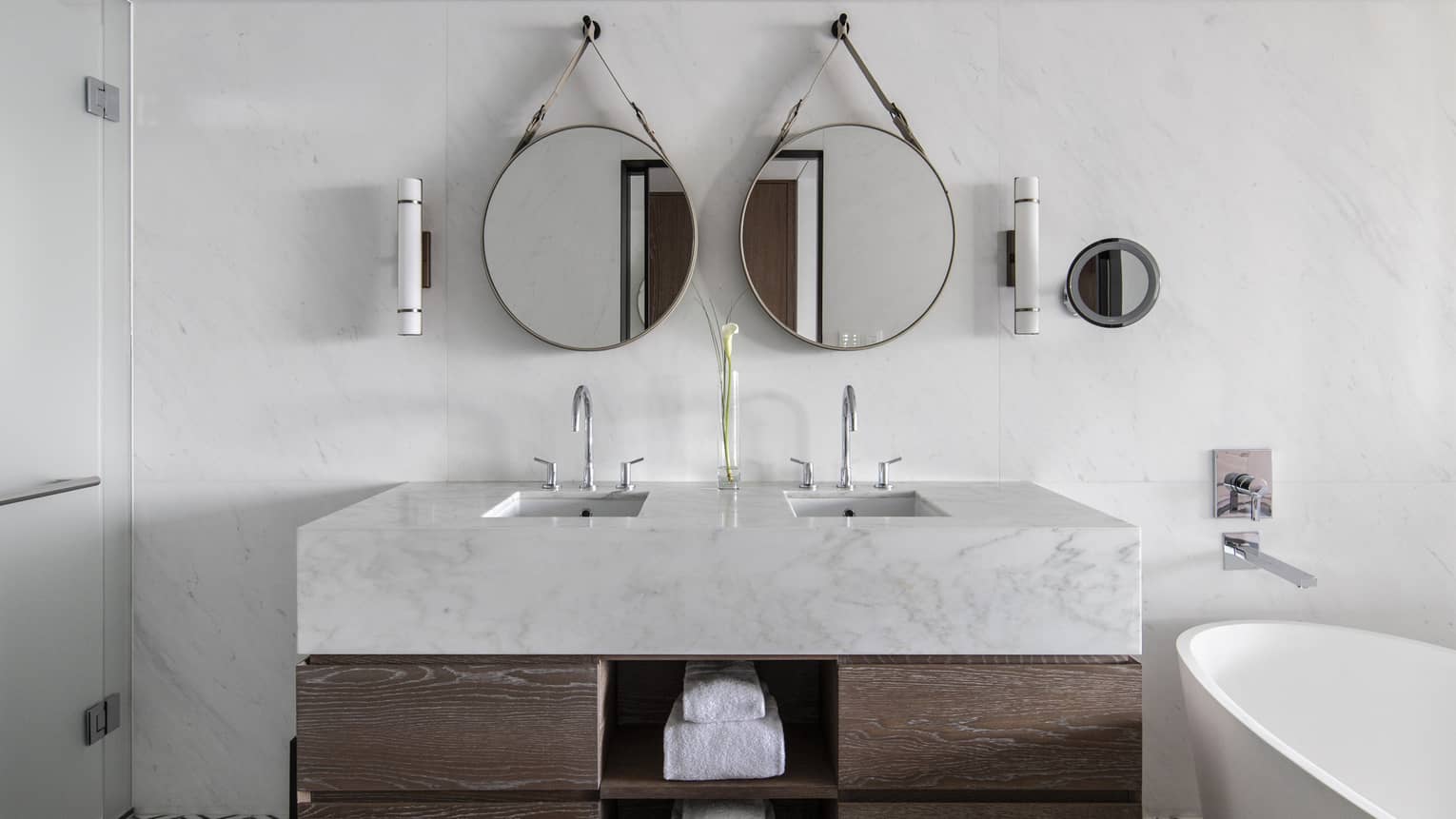Bathroom with marble and wood vanity, two round mirrors, white tub