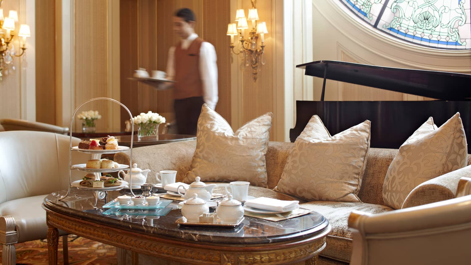 Formal tea service, sandwiches and dessert on table in front of white satin sofa 