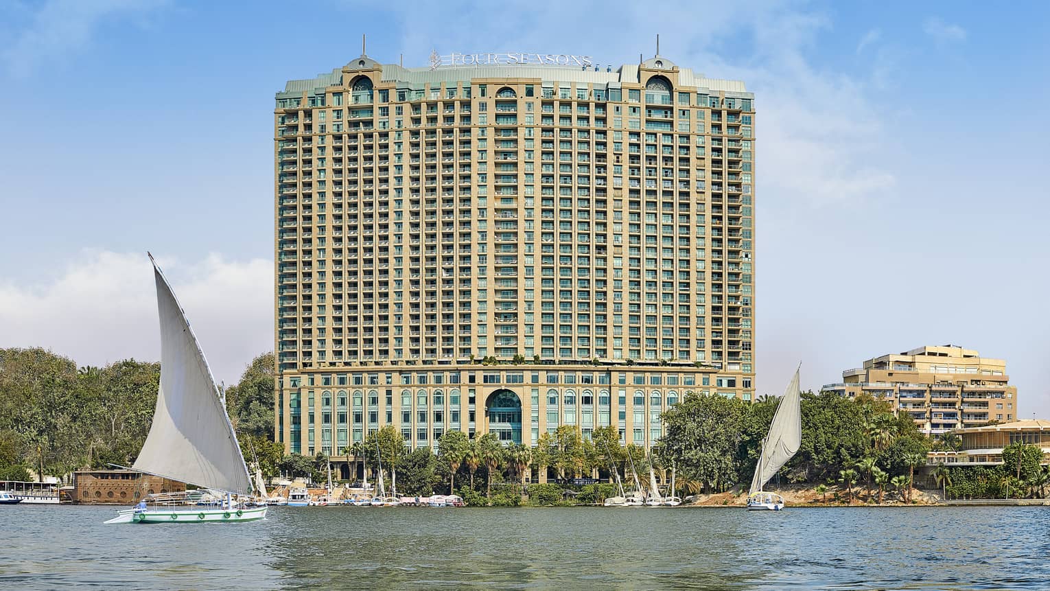 Exterior shot of a large hotel building on the water, sail boats can be seen in the foreground.