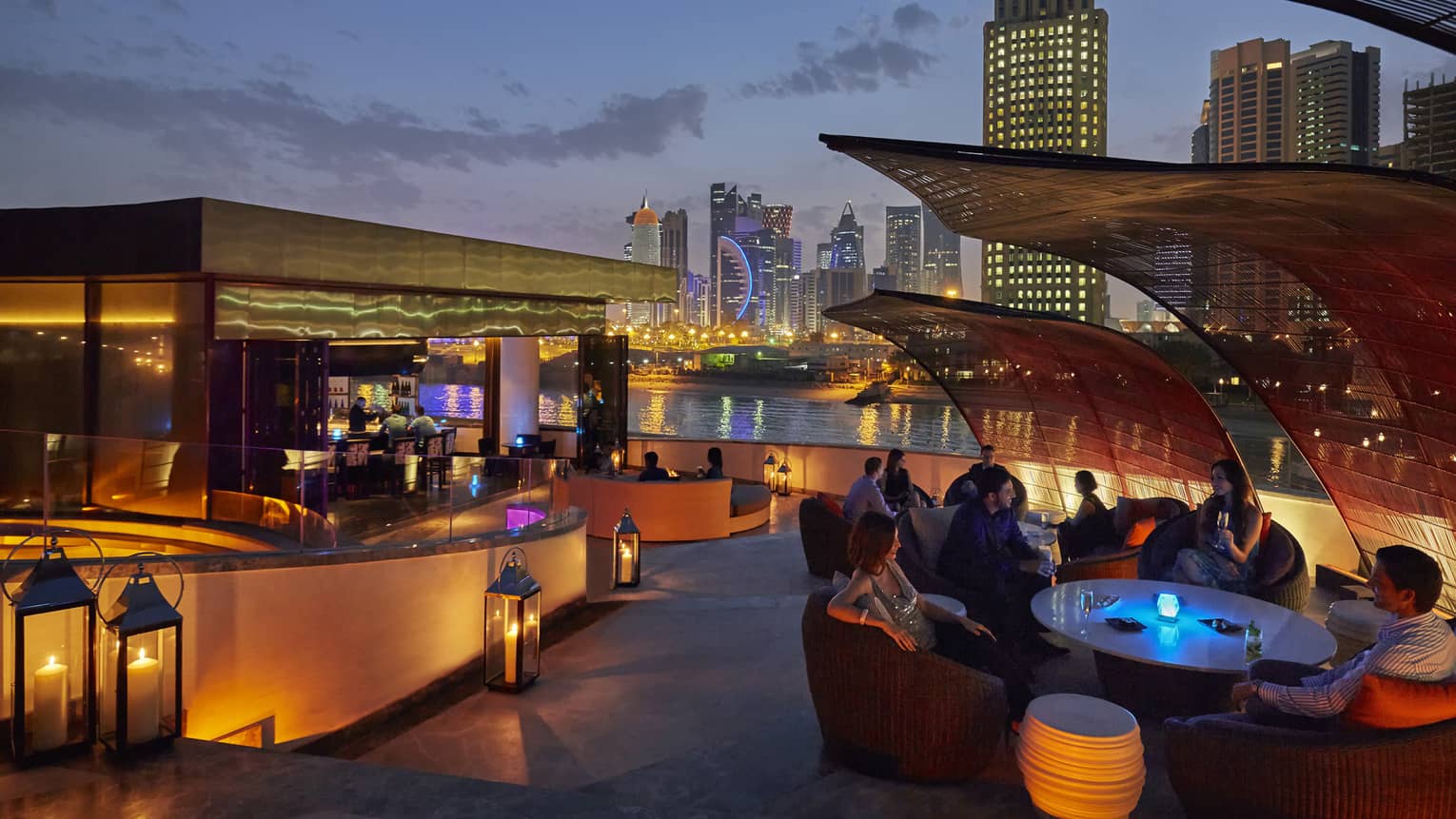 Nobu Doha patio at night with glowing lanterns around bar, table, city skyline in background